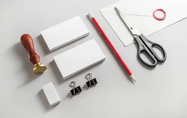 Berbagai alat desain dan percetakan, termasuk cutter, pensil, stempel, dan klem.