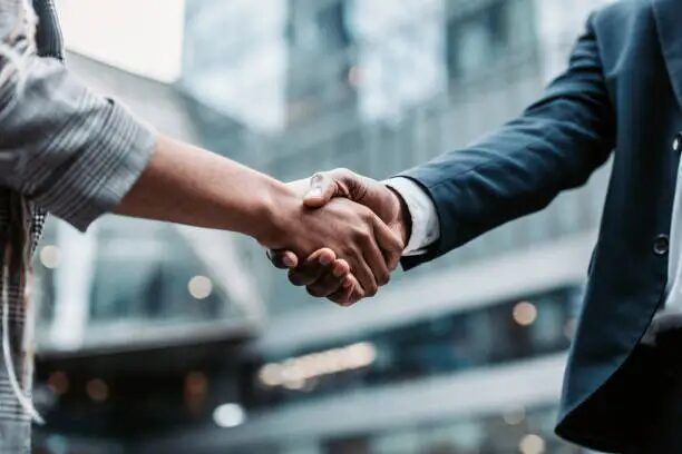 Tangkapan tangan antara dua orang di latar bangunan modern, simbol kerjasama bisnis.