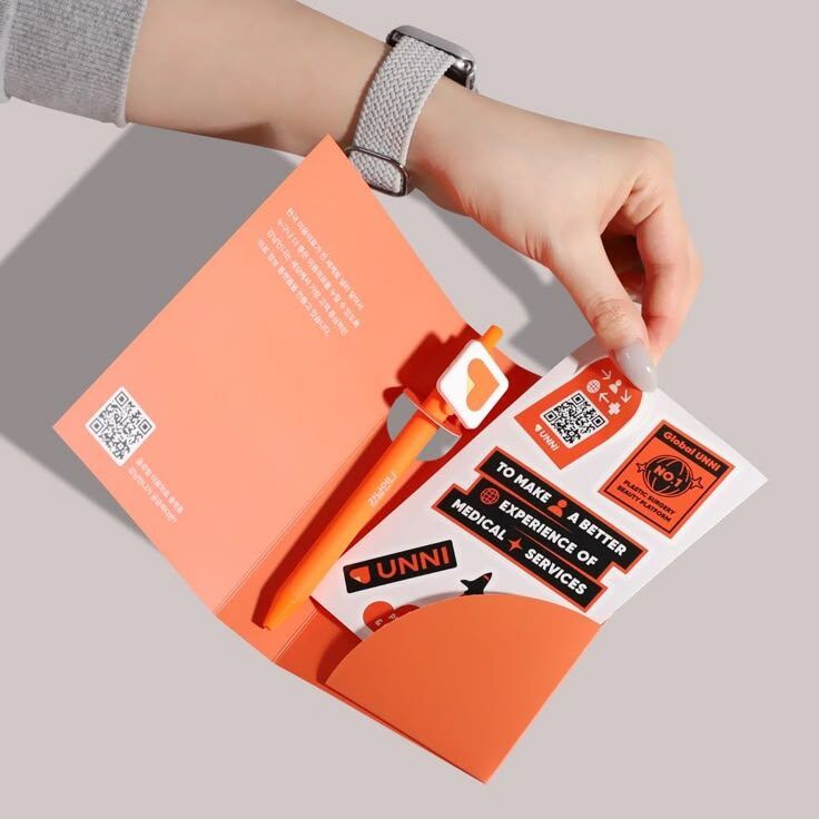Tangan memegang kartu promosi UNNI dengan pen dan stiker.