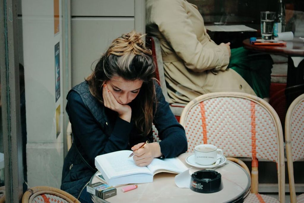 Perempuan menulis di meja cafe dengan buku dan pena.