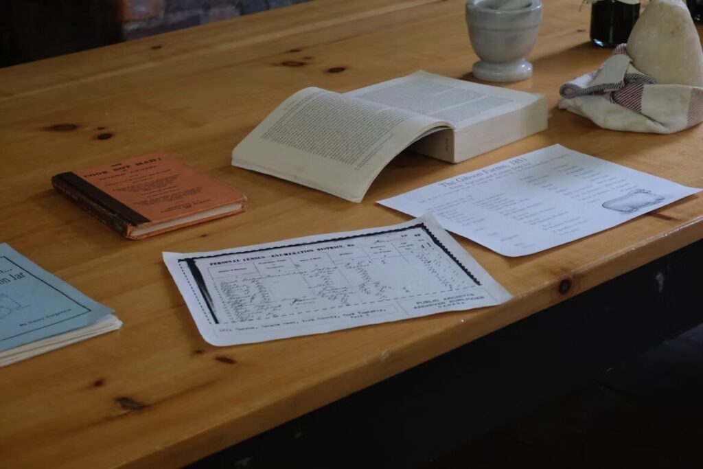 Meja kayu dengan buku terbuka, surat, dan kertas yang menggambarkan persiapan file cetak dan distribusi kalender meja.