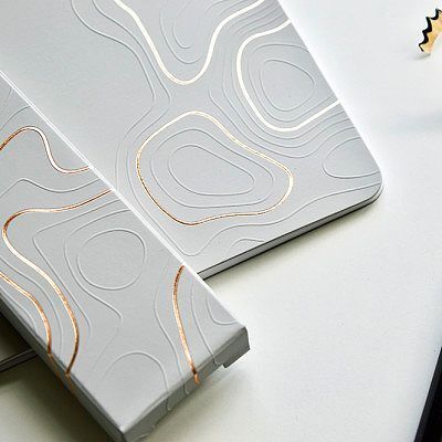 Buku hardcover putih dengan desain topografi emas, cocok untuk promosi branding.