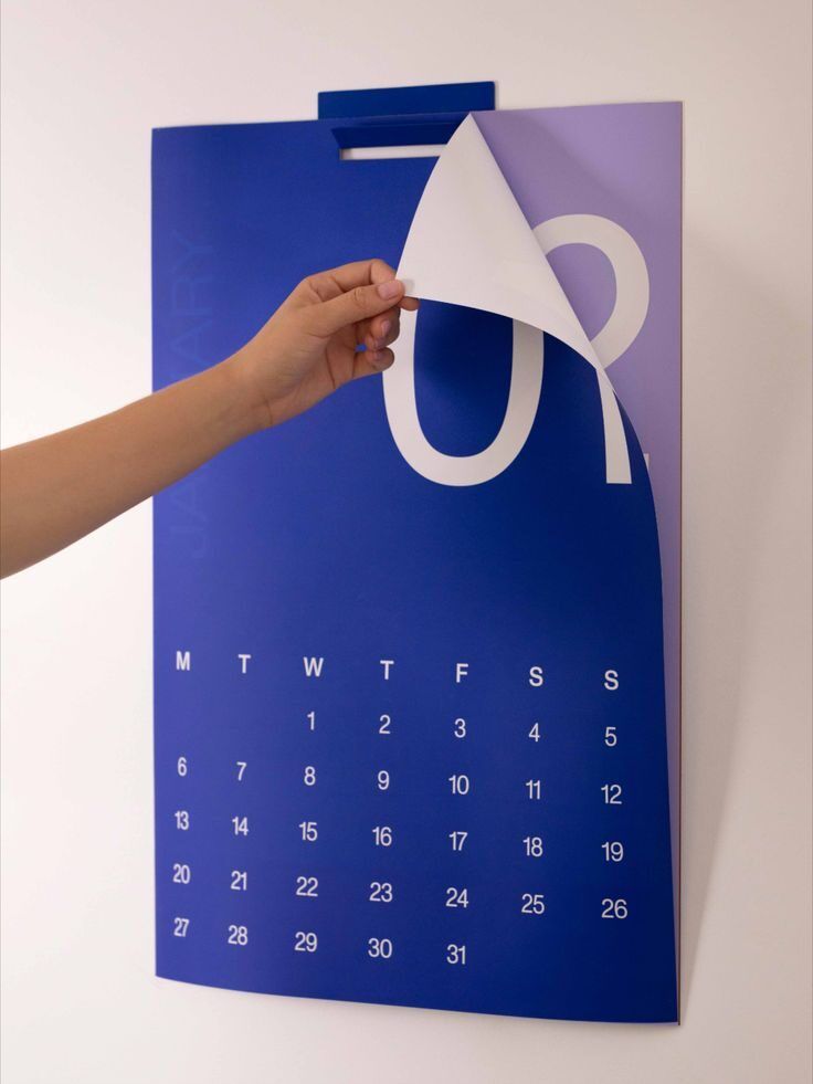 Tangan memegang lembaran baru dari kalender biru dengan desain modern.