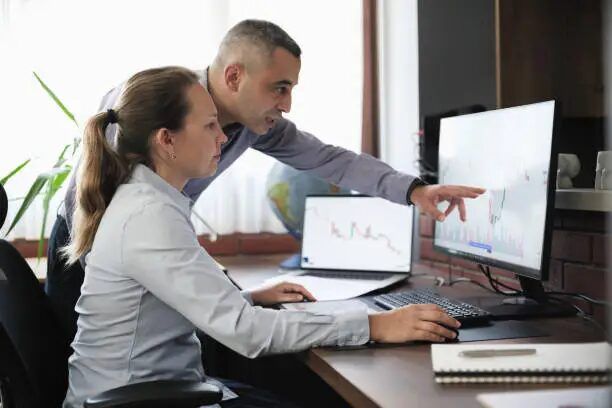 Dua orang sedang melihat grafik di layar komputer di kantor.