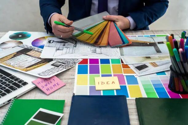 Meja kerja dengan palet warna, sketsa, dan alat desain, menunjukkan proses perencanaan desain interior.