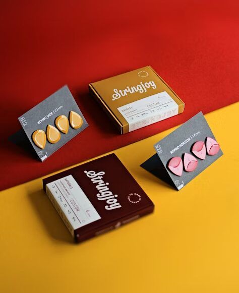 Paket alat musik Stringjoy dengan berbagai ukuran dan warna di atas latar merah dan kuning.