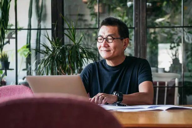 Pria berkerudung duduk di meja cafe, fokus pada laptopnya.