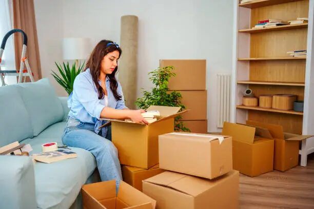 Woman organizing cardboard boxes in a living room during a move.