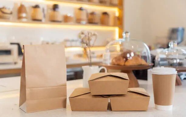 Paket makanan dan minuman dalam kemasan kertas di meja kafe.
