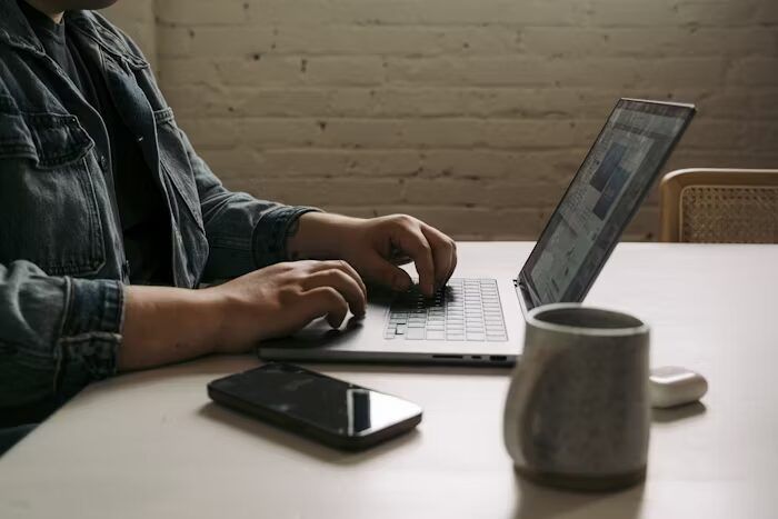 Tangan sedang mengetik pada laptop di meja dengan peralatan perkantoran.