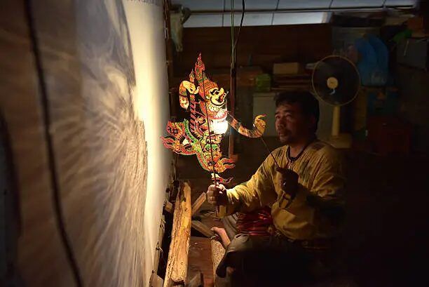 Pekerja menunjukkan wayang kulit di ruang kerja yang gelap.