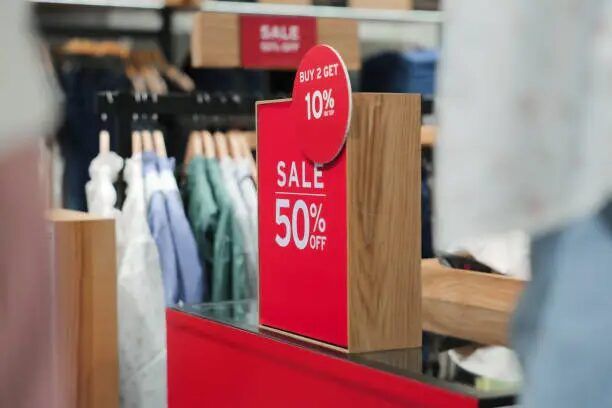Tanda promosi diskon 50% di toko pakaian dengan latar belakang rak pakaian