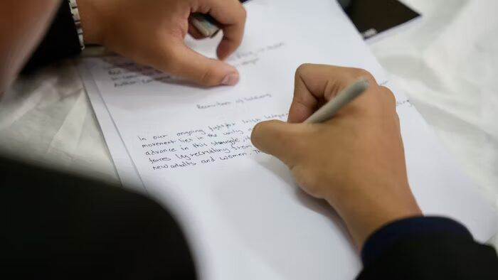 Tangan menulis di lembaran kertas putih dengan pena