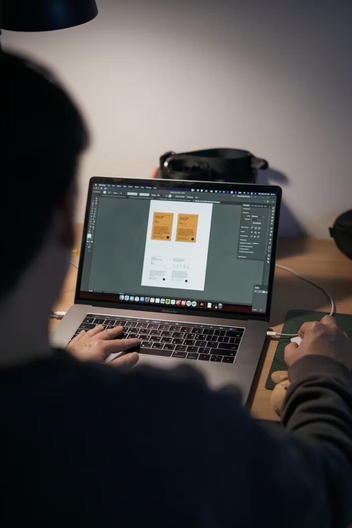 Orang sedang menggunakan laptop untuk desain grafis dengan aplikasi Adobe.