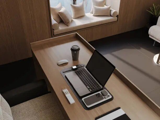 Meja kerja minimalis dengan laptop, mouse, dan aksesori di ruang kerja modern.