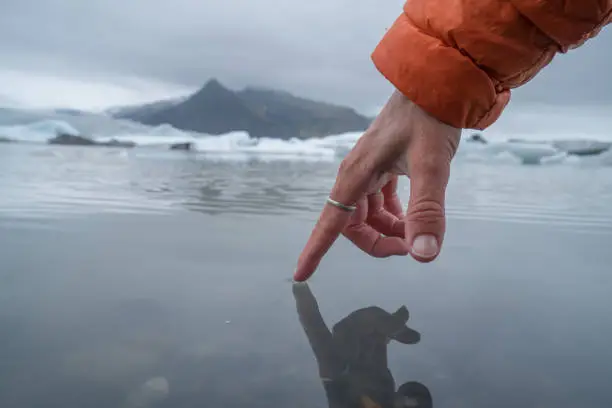 Tangan memegang air di pantai dengan latar gunung dan es.
