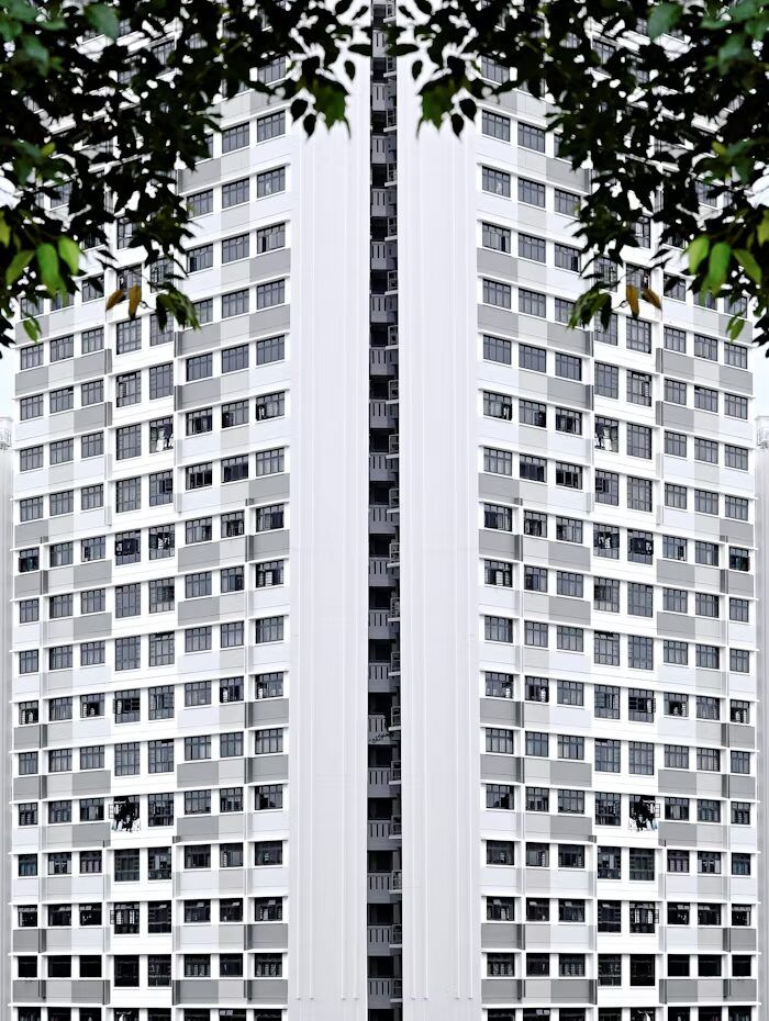 Gambar depan bangunan apartemen modern dengan banyak jendela dan struktur monolitik.