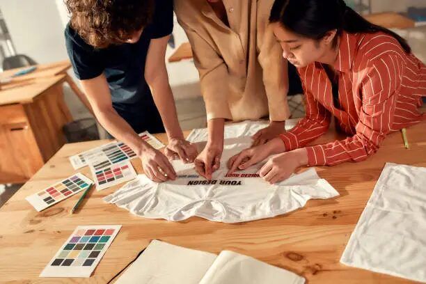Tiga orang desainer sedang bekerja sama meninjau tata letak desain bahan promosi sebelum masuk proses cetak.