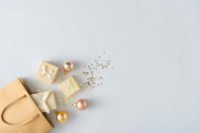Paket hadiah Natal dengan ornamen emas dan konfetti di atas tas kertas cokelat.