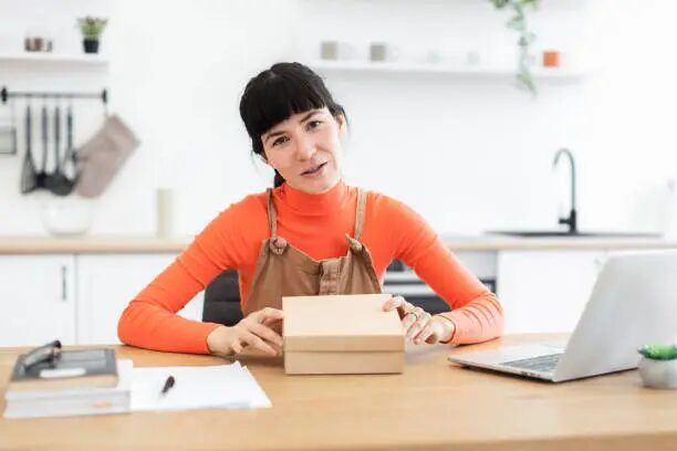 Perempuan memegang kotak hadiah di meja dengan laptop di sampingnya.