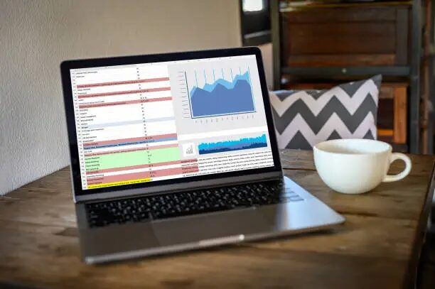 Laptop menampilkan grafik dan data analitik di layar, di meja dengan cangkir kopi.