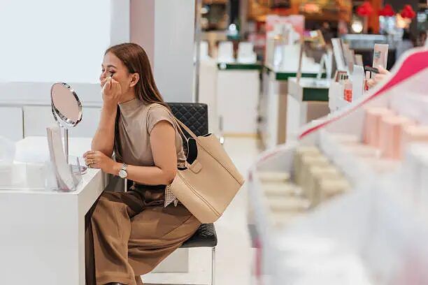Perempuan sedang mencoba makeup di depan cermin di toko kosmetik.
