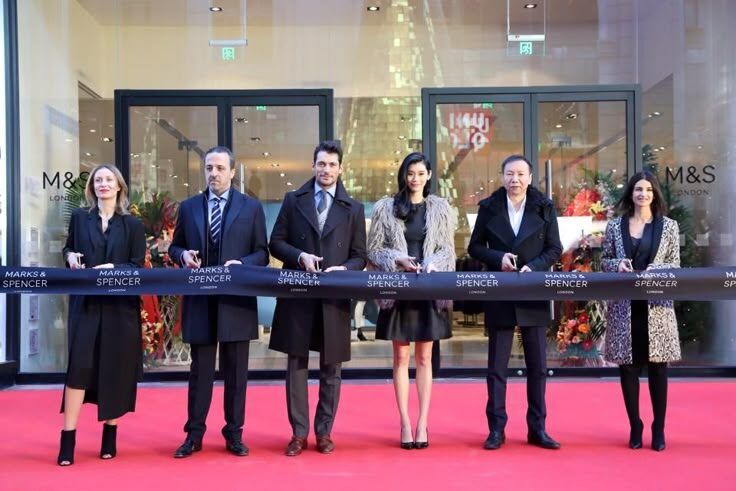 Grup orang menyeberangkan pita merah di depan toko Marks & Spencer.