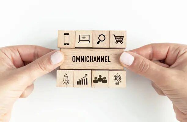 Tangan memegang blok kayu dengan ikon dan kata 'OmniChannel'.