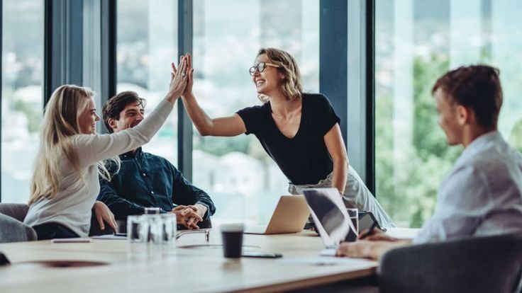 Tiga orang sedang saling memberi high five di ruang rapat modern.