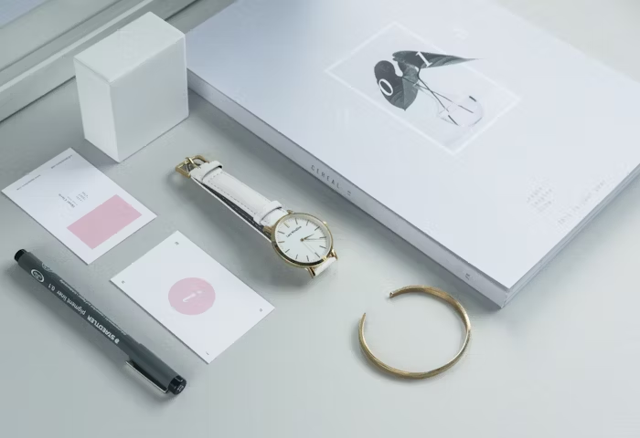 Tampilan minimalis dengan jam tangan, pensil, dan benda-benda cetak.