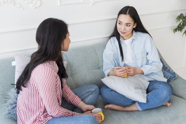 Dua wanita berbincang di sofa, suasana santai dan hangat.