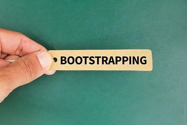 Tangan memegang kartu dengan tulisan 'BOOTSTRAPPING'