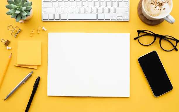 Meja kerja dengan kertas kosong, keyboard, dan gadget.