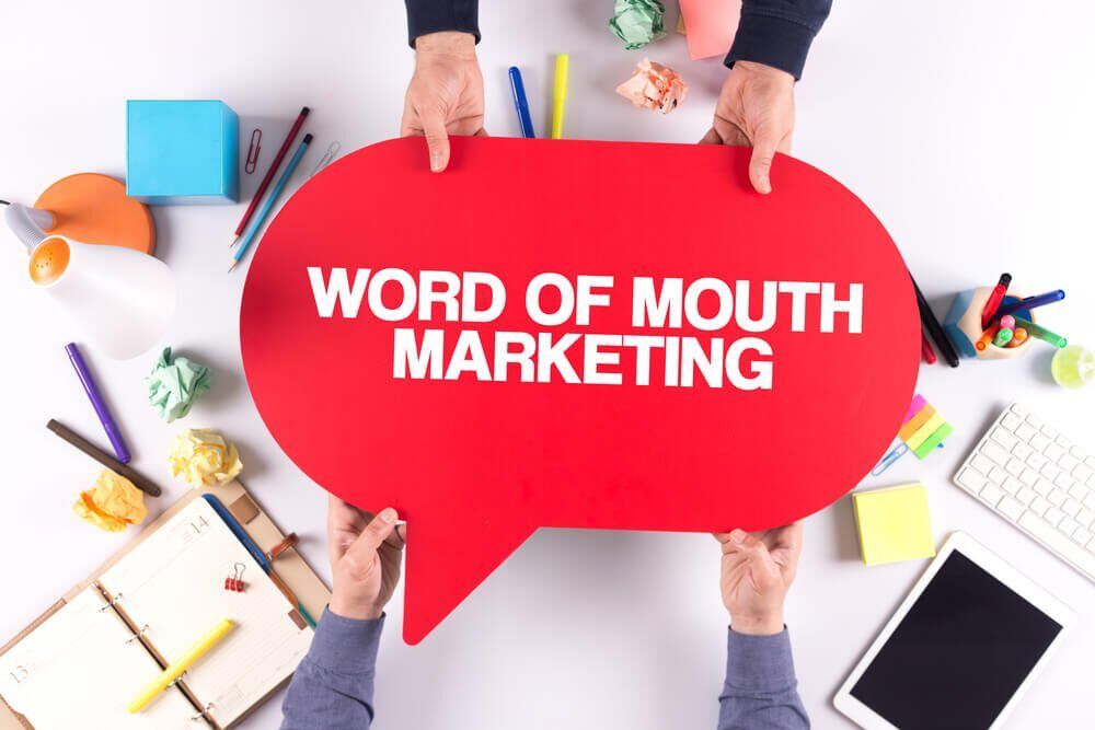 Tangan membentuk balon kata-kata merah Word of Mouth Marketing di meja kerja sebagai ilustrasi strategi word of mouth marketing