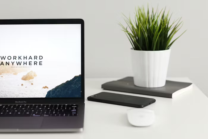 Laptop, mouse, potted plant, dan smartphone di meja kerja minimalis