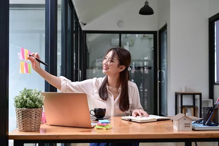 Perempuan sedang merancang dengan kertas warna dan laptop di kantor modern.