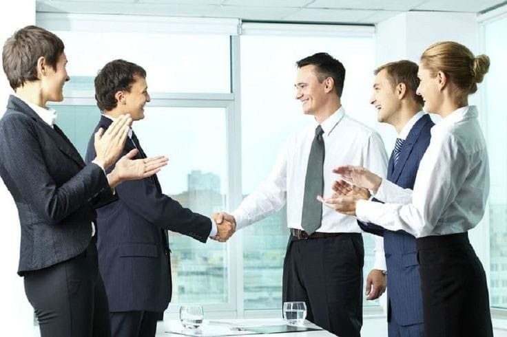 Empat orang sedang berjabat tangan dalam ruang kantor modern.