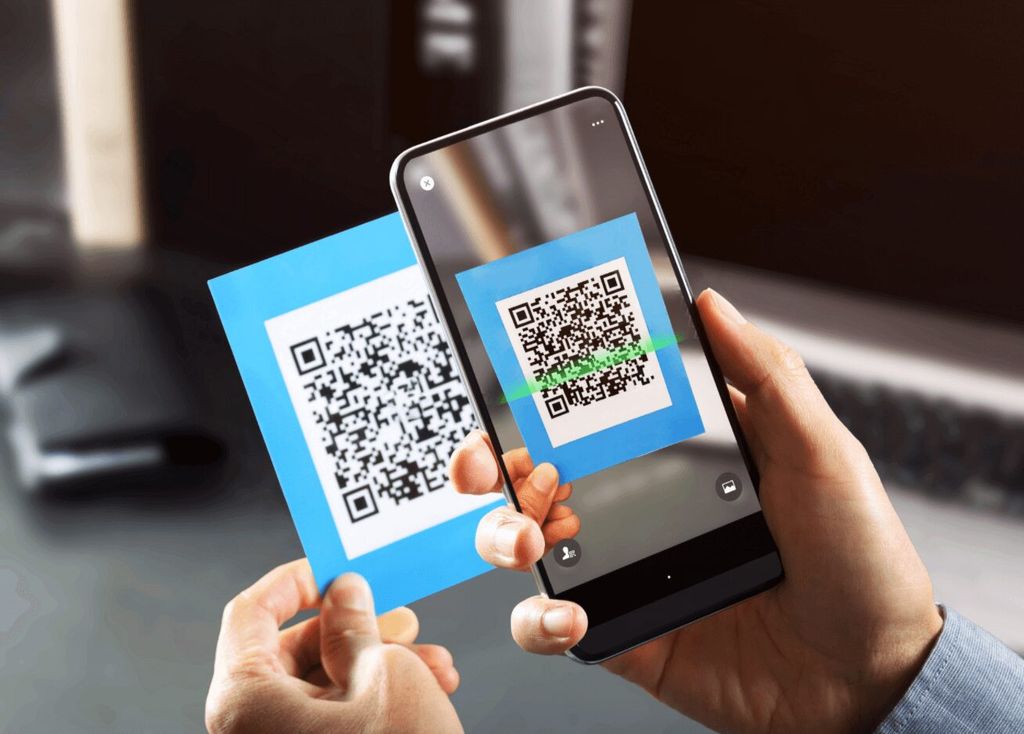 Tangan memegang kartu berQR dan smartphone sedang melakukan scan QR Code.