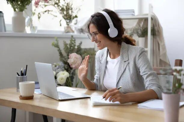 Perempuan sedang melakukan video call di meja kerjanya dengan laptop dan headset.