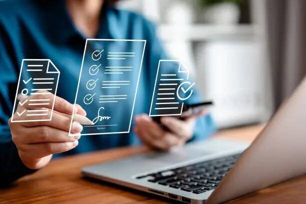Tangan memegang laptop dan dokumen virtual, menunjukkan proses penggunaan aplikasi percetakan online.