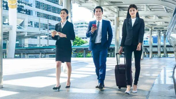 Tiga orang pekerja dalam pakaian kerja profesional di depan gedung perkantoran.