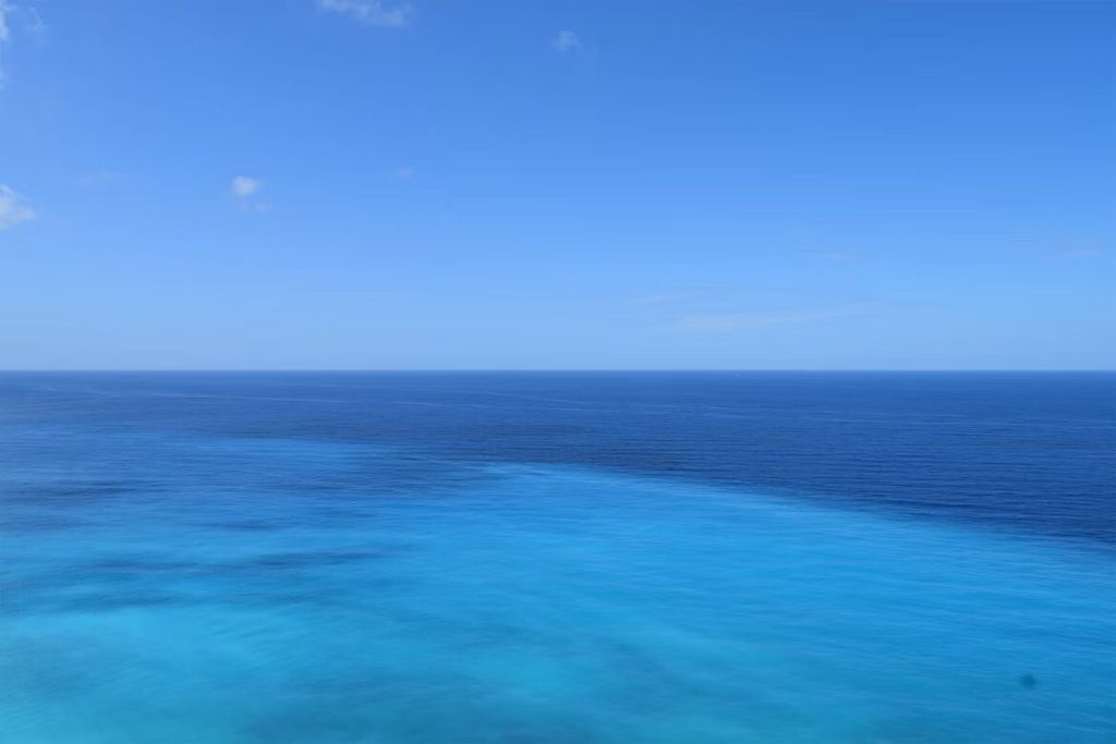 Pemandangan laut biru luas dan tenang dengan langit cerah.