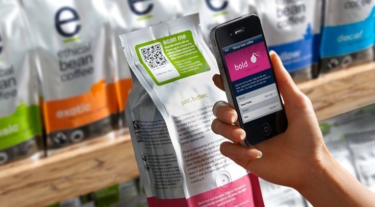 Tangan memegang smartphone dengan aplikasi Ethical Bean Coffee dan kemasan kopi di latar belakang