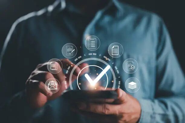 Tangan memegang smartphone dengan ikon ceklist dan dokumen yang muncul.