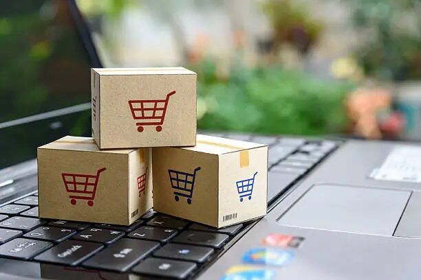 Tiga kotak karton berukuran kecil dengan simbol belanja di atas keyboard laptop.