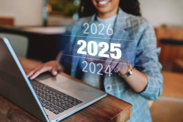 Tangan memegang laptop dengan tampilan tahun 2024-2026 di layar.