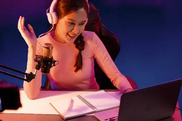 Perempuan sedang streaming game di studio dengan laptop dan mikrofon.