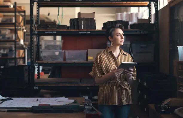 Perempuan memegang tablet di gudang dengan rak dan peralatan