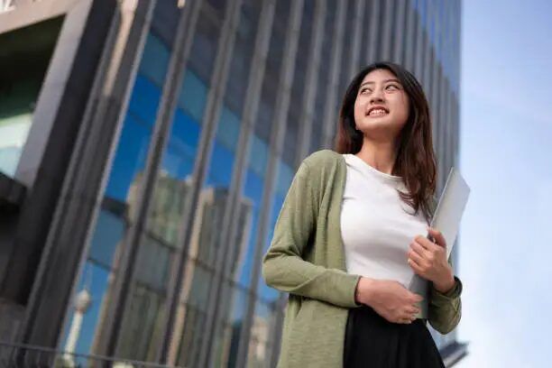 Perempuan memegang buku di depan bangunan modern