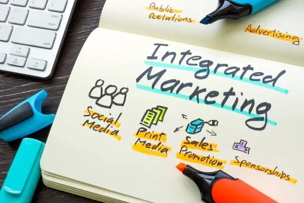 Buku terbuka dengan tulisan 'Integrated Marketing' dan elemen visual promosi.